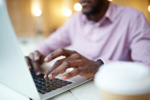 Man in purple shirt types on a laptop keyboard.